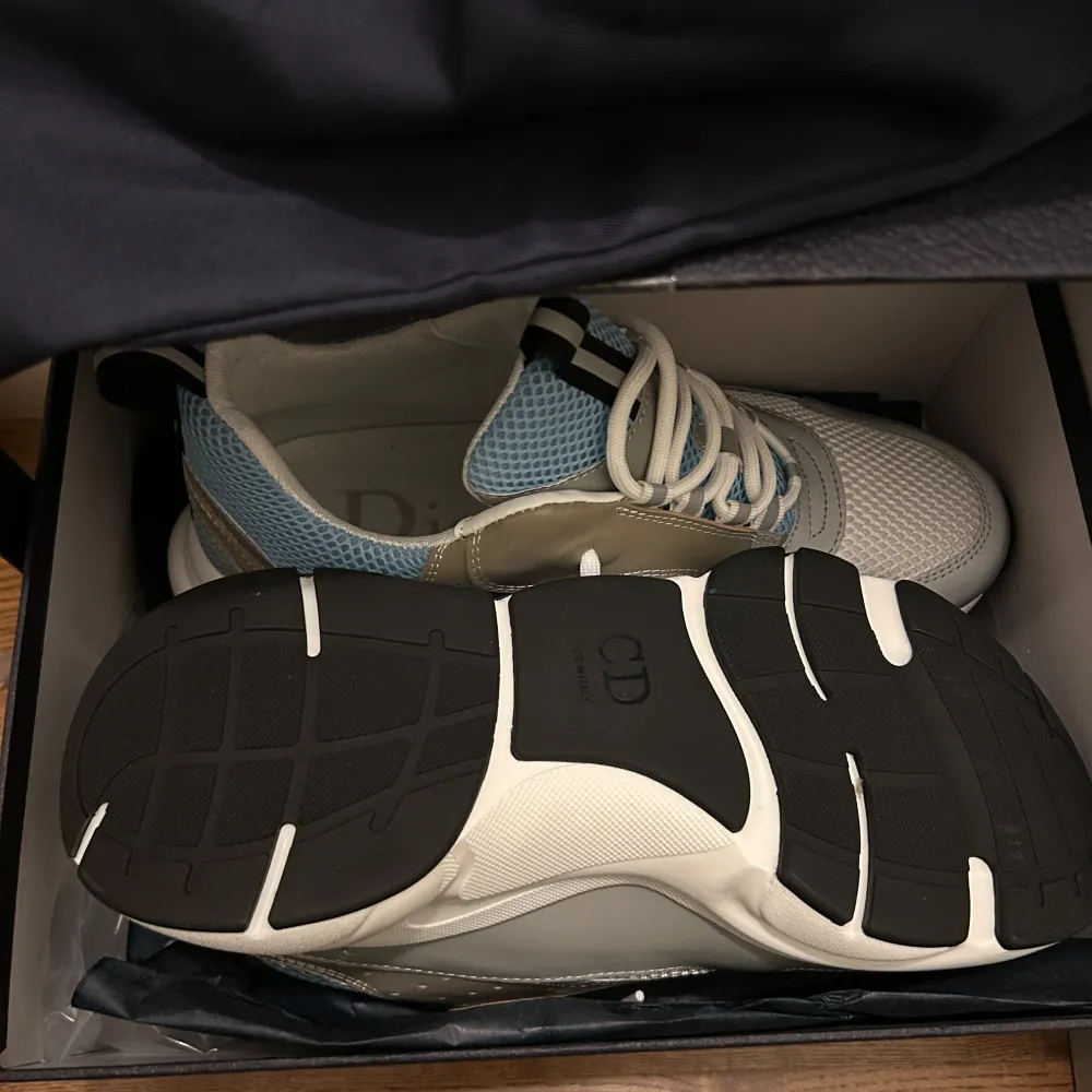 Snygga sneakers från Dior i en kombination av blått, grått och vitt. Skorna har en modern design med snörning och en bekväm sula. Perfekta för en stilren look.. Kengät.