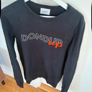 Svart tröja från Dondup - Snygg svart tröja från Dondup med tryck i vitt och rött. Tröjan har långa ärmar och en rund halsringning. Perfekt för en stilren look. Tröjan är använd och har tecken på det. Passar S/M
