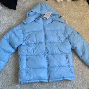 Ljusblå dunjacka från Moncler - Säljer en snygg oanvänd ljusblå dunjacka från Moncler med huva och dragkedja. Jackan har långa ärmar och praktiska fickor med dragkedja. Perfekt för kyliga dagar! Har fungerande nfc tag. Säljer då den va för stor för mig 