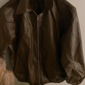 Brun skinnjacka med dragkedja - Snygg brun skinnjacka (PU) med dragkedja och klassisk krage. Perfekt för en stilren look. Jackan har en oversized passform, perfekt för vår/höst. 