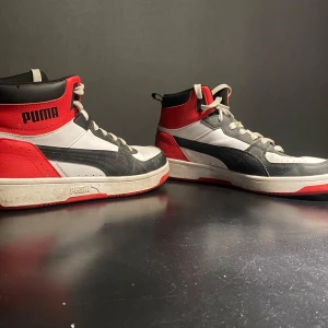 Puma sneakers i rött, svart och vitt - Snygga Puma sneakers i en cool färgkombination av rött, svart och vitt. Skorna har en hög modell med snörning och en robust sula. Perfekta för en sportig look.