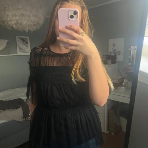 Svart blus med spetsdetaljer - Snygg svart blus med transparenta partier och spetsdetaljer. Blusen har korta ärmar och en luftig passform, perfekt för en stilren look. Den är tillverkad i ett lätt och bekvämt material. Väldigt lik by malina blusen fast denna är från happyholly. Storlek 36/38.