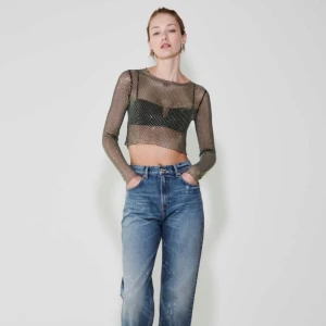 Svart mesh topp - Trendig svart mesh topp med långa ärmar och croppad design. Perfekt för en kväll ute med vänner. Toppen har ett glittrigt mönster som ger en extra touch av glamour.