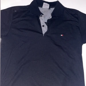 Svart pikétröja från Tommy Hilfiger - Snygg svart pikétröja från Tommy Hilfiger. Den har en liten logotyp på bröstet och är perfekt för en stilren look. Piken är i skicket 9/10 Den kostar 500kr ny