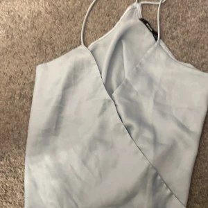 Ljusblå omlottklänning från Bik Bok - Snygg ljusblå omlottklänning från Bik Bok med smala axelband. Perfekt för en stilren look. Klänningen har en elegant omlottdesign som ger en fin passform.