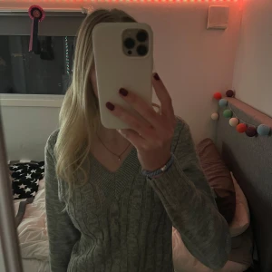 Grå stickad tröja - Säljer en mysig grå stickad tröja med v-ringning och kabelstickat mönster. Tröjan är croppad och har långa ärmar.