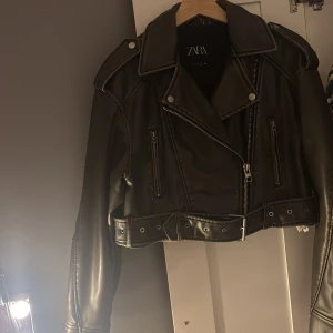 Grön skinnjacka från Zara - Snygg grön skinnjacka från Zara med dragkedja och knappar. Jackan är croppad och har ett bälte i midjan för extra stil. Nypris 850kr säljer för 450