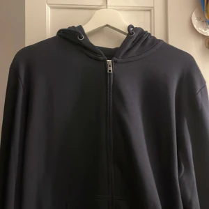 Mörkblå hoodie med dragkedja - Säljer en stilren mörkblå hoodie med dragkedja och huva. Perfekt för en avslappnad look. Den har långa ärmar och en klassisk passform.