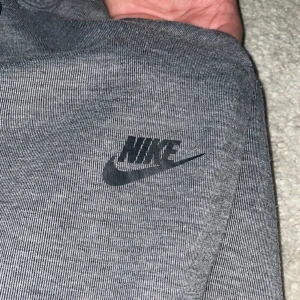 Grå mjukisbyxor från Nike HERR - Snygga grå mjukisbyxor från Nike med svart logga på låret. Byxorna har snörning i midjan och ribbade muddar vid bensluten för en bekväm passform. Dom är i storlek M köpta förra året, andvända knappt 2 gånger så de är som nya! Nypris 800. Vårt pris 600kr men går självklart att diskuteras!😊