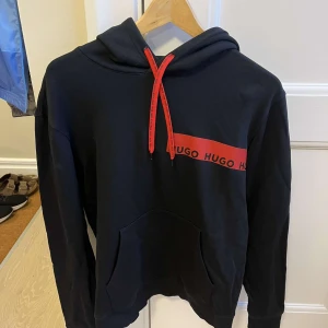 Svart hoodie från Hugo Boss - Snygg svart hoodie från Hugo Boss med röd logga och matchande byxor till. Inga slitage tecken, pris kan diskuteras men ca 650kr