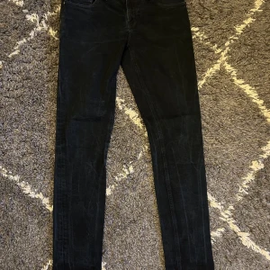 Svarta skinny jeans från Nudie Jeans - Snygga svarta slim jeans från Nudie Jeans i storlek 31/32. Tillverkade av 98% ekologisk bomull och 2% elastan för en bekväm passform. Perfekta för en stilren look. Köptes för 1499 och säljs här för 449