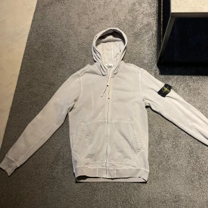 Stone Island hoddie - Säljer en vit hoodie från Stone Island med dragkedja och huva. Finns en liten lagning vid armbågen annars i bra skick. Storlek M