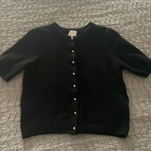 Svart kofta med knappar - Snygg svart kofta med korta ärmar och eleganta knappar framtill. Perfekt för en stilren look. Köpt för 200 på hm! Använd cirka 3 gånger! Inga defekter! Säljer även en i vit!