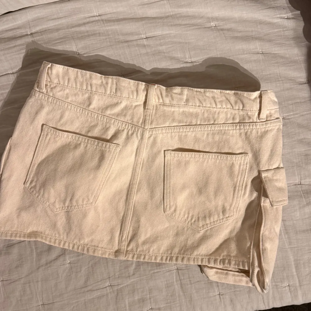 Snygg beige kortkjol från Blue Denim med praktiska fickor och en cool design. Kjolen har en dragkedja fram och en unik fickdetalj på sidan. Perfekt för en avslappnad stil.. Hameet.