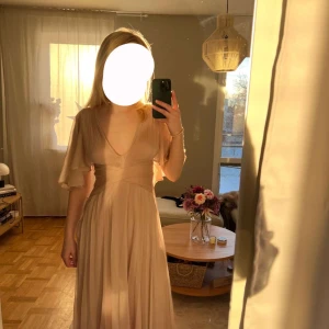 Champagnefärgad långklänning - Elegant champagnefärgad långklänning med v-ringning och volangdetaljer på ärmarna. Klänningen har en omlott-design och knappar i ryggen, vilket ger en romantisk touch. Perfekt för speciella tillfällen.Balklänning från Asos, endast använd en gång!  Klänningen är champagne färgad mot det rosa hållet Nypris på Asos hemsida är 1200 kr🩷🥂 Kunna ej knäppa knapparna i bak, därför de är öppna. Inga defekter   Den passar perfekt på mig och MINA mått är:  Byst : 84cm Midja : 62cm  Längd : 168cm