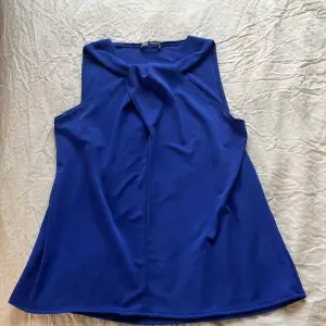 Säljer en stilren blå ärmlös topp från Zara. Toppen har en elegant drapering framtill och är tillverkad i ett mjukt material. Perfekt för en chic och bekväm look.