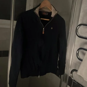 Mörkblå Morris full zip tröja - Snygg mörkblå Morris full zip med med ett litet broderat Morris emblem på bröstet. Perfekt för en stilren look. Tröjan har långa ärmar och en klassisk krage. Pris 749, ny pris 2000, storlek S, väldigt bra skick, använd ett fåtal gånger!