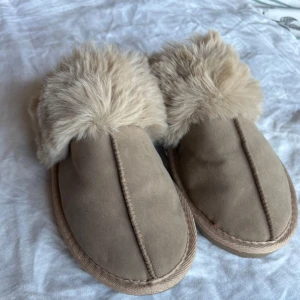 Beige tofflor med pälsfoder, inte använda Gina Tricot - Mysiga beige tofflor med mjukt pälsfoder. Perfekta för att hålla fötterna varma under kalla dagar. Sulan har ett bra grepp och storleken är 36/37. Aldrig använda då jag fick ett par tofflor samma dag i julklapp. Från Gina Tricot