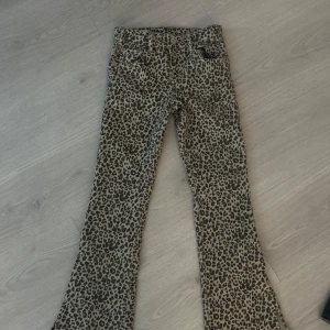 Leopardmönstrade byxor - Snygga leopardmönstrade byxor med bootcut-stil. Perfekta för att ge en djärv touch till din outfit. Byxorna har en klassisk passform och är tillverkade i ett bekvämt material. storlek barn 134