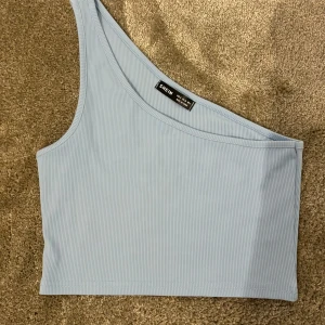 Ljusblå oneshoulder topp från SHEIN - Snygg ljusblå oneshoulder topp från SHEIN i ribbat material. Perfekt för en stilren look med en unik asymmetrisk design. Toppen är i storlek S. 