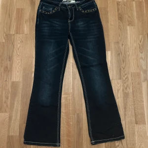 Bootcut jeans - Snygga mörkblå bootcut jeans från John Baner med dekorativa sömmar och detaljer på bakfickorna. Jeansen har en klassisk femficksdesign och knappar med mönster. De är använda med lite slitningar på fickorna (bild 3).
