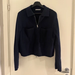 Mörkblå cardigan med dragkedja - Snygg mörkblå cardigan från åhlens med dragkedja framtill och två stora fickor. Jackan har en klassisk krage och långa ärmar, perfekt för en stilren look.