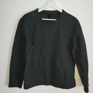 Mörkgrå tröja från H&M - Säljer en stilren mörkgrå tröja från H&M. Tröjan har en klassisk rund hals och långa ärmar, perfekt för en avslappnad look. Tillverkad i ett mjukt material som ger en bekväm passform.