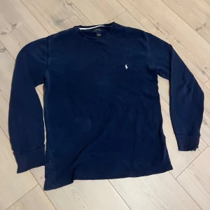 Mörkblå långärmad tröja från Polo Ralph Lauren - Säljer en stilren mörkblå långärmad tröja från Polo Ralph Lauren. Tröjan är i bomull och har en liten broderad logotyp på bröstet. Perfekt för en avslappnad och klassisk look. Den är i bra skick, ett litet hål på armbågen men inget man tänker på storleken är L men kan passa M