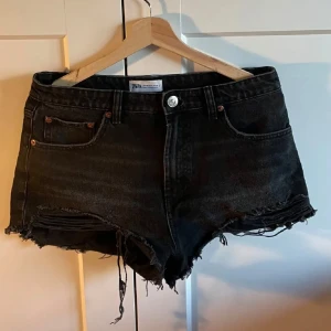 Svarta jeansshorts från Zara - Snygga svarta jeansshorts från Zara med fransiga kanter och klassisk femficksdesign. Perfekta för en avslappnad stil med en t-shirt eller linne. De har en knapp och dragkedja framtill för enkel påklädning. Storlek 40 men ganska små så passar S/M