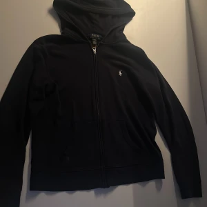 Mörkblå zip hoodie från Polo Ralph Lauren - Säljer en snygg mörkblå hoodie från Polo Ralph Lauren med dragkedja och det klassiska logotypbroderiet på bröstet. Perfekt för en avslappnad stil. Den har en praktisk huva och långa ärmar.
