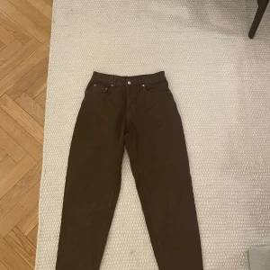 Bruna jeansbyxor - Snygga bruna jeansbyxor med klassisk femficksdesign. Byxorna har en rak passform och är perfekta för en avslappnad stil. De har en knappgylf och bälteshällor för extra funktionalitet.