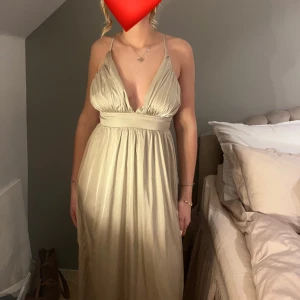 Champagnefärgad långklänning med öppen rygg - Elegant champagnefärgad långklänning med djup v-ringning och smala axelband som korsas i ryggen. Klänningen har en markerad midja och ett flytande fall som ger en vacker siluett. Perfekt för speciella tillfällen. 🤍🤍🤍 klänningen är använd 1 gång och är nyskick utan prislapp bara. Passar alla längder mellan 1,55 - 173 cm ❤️