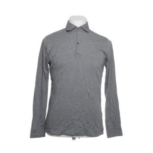 Grå pikétröja från Massimo Dutti - Snygg grå pikétröja från Massimo Dutti i 100% merceriserad bomull. Tröjan har långa ärmar och en klassisk krage med knappar framtill. Perfekt för en stilren look.