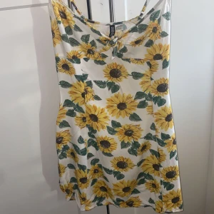Blommig sommarklänning H&M - Söt sommarklänning från H&M med solrosmönster. Klänningen är ärmlös och har en avslappnad passform, perfekt för varma dagar. Den är gjord i ett lätt och luftigt material med en vit bas och gula blommor. Använd 1/2 gånger.