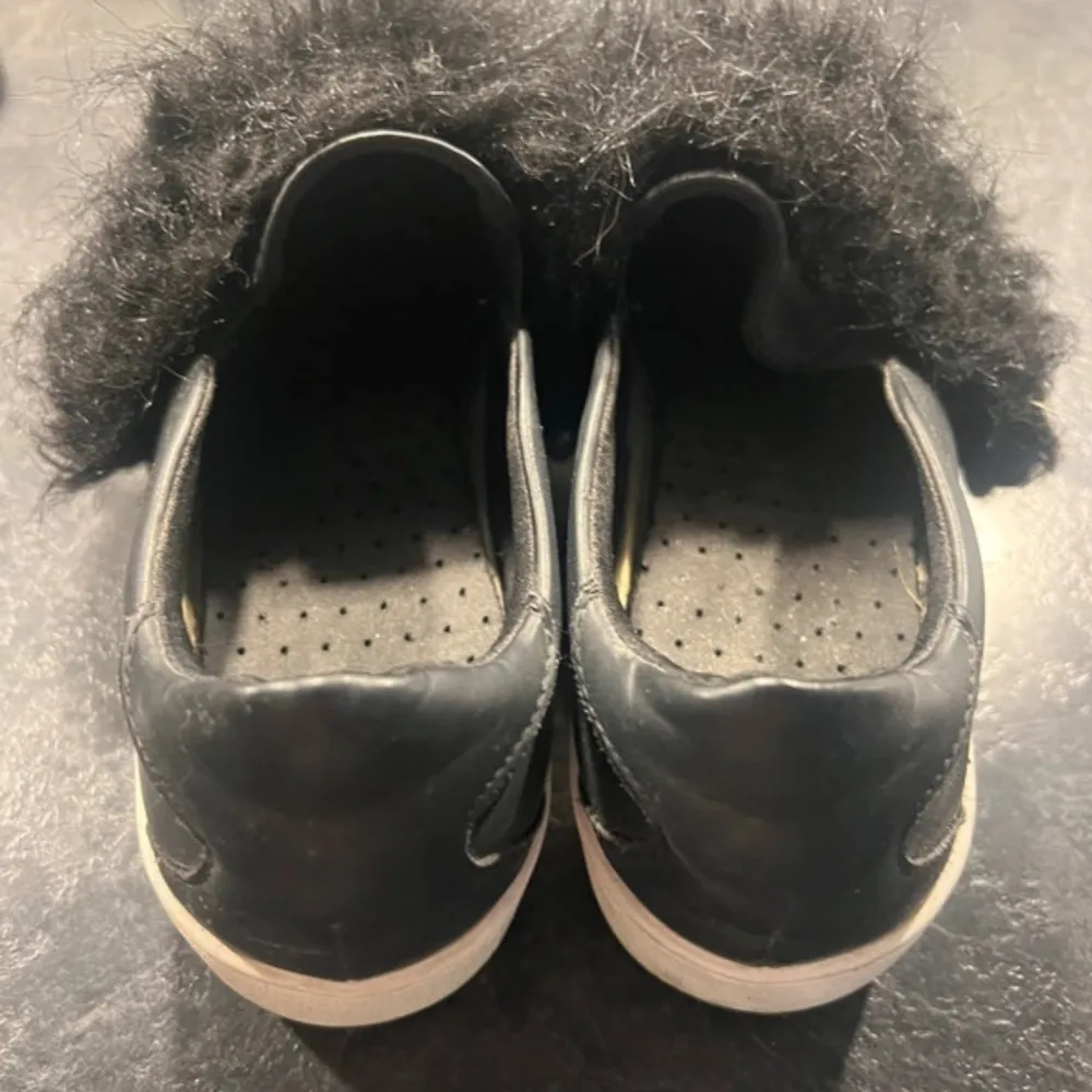 Snygga svarta sneakers med en unik pälsdetalj på ovansidan. Skorna har en vit sula som ger en fin kontrast till det svarta. Perfekta för att ge din outfit en trendig touch.. Kengät.