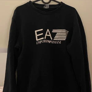 Svart tröja från Emporio Armani - Snygg svart tröja från Emporio Armani med EA7-logga på framsidan. Tröjan har långa ärmar och en rund halsringning. Pris kan diskuteras!😊💗