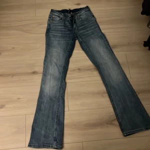 Blå bootcut jeans - Säljer ett par klassiska blå bootcut jeans med låg midja. De har en snygg tvättad look och femficksdesign. Perfekta för en avslappnad stil.