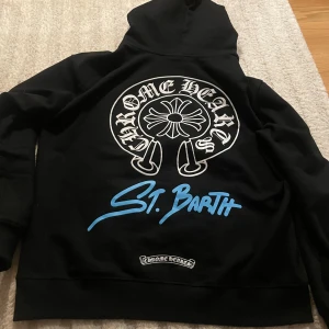  Chrome Hearts Hoodie - Hej!!😁 Säljer en svart hoodie från Chrome Hearts med en fet dragkedja och tryck på både fram- och baksid🔥. Hoodien har en stor logga på ryggen och texten 'St. Barth' i blått. Tillverkad i 100% bomull och har en bekväm passform.🤩🤩VID SNABB AFFÄR -BÄTTRE PRIS!!!!!
