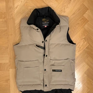 Canada goose väst - Canada Goose väst i en fin beige färg strl xs men passar som S. Riktigt fint skick. Västen är såklart äkta!