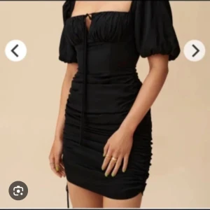 Svart klänning från ADOORE - Snygg svart klänning från ADOORE med puffiga kortärmar och en åtsittande passform. Klänningen har en knytning framtill och rynkade detaljer längs sidorna som ger en smickrande siluett. Perfekt för en kväll ute eller en speciell tillställning. Helt ny!