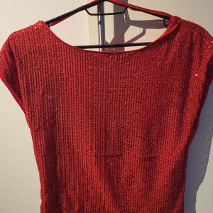 Röd glittrig topp - Snygg röd glittrig topp med korta ärmar och rund halsringning. Perfekt för en festlig kväll.