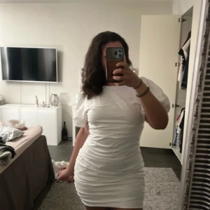 Vit kort klänning med puffärm - Säljer en stilren vit kort klänning med puffärmar. Klänningen har en tight passform och är perfekt för sommarens alla tillfällen. Den är tillverkad i ett lätt och bekvämt material som ger en smickrande silhuett. Men också perfekt inför studenten