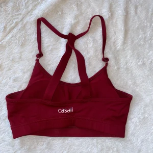 Vinröd sporttopp från Casall - Snygg vinröd sporttopp från Casall med korsade axelband och justerbara remmar. Perfekt för träning med en bekväm passform och stilren design.