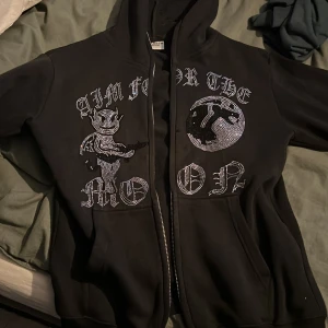Svart hoodie  - Säljer en svart hoodie från Aim for the Moon. Säljer för den har blivit liten för mig men väldigt bra skick alla stenar sitter kvar.
