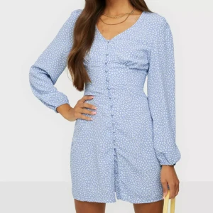 Blommig blå klänning med knappar - Säljer en söt blå klänning med små vita blommor och knappar framtill. Klänningen har långa ärmar och en v-ringad hals. Perfekt för en somrig look! 🌸 klänningen är från Nelly, har använt en gång och säljer den därav