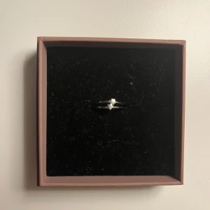 Silverfärgad ring med stjärndetalj - Elegant silverfärgad ring med en liten stjärndetalj i mitten. Ringen har en enkel och stilren design som passar perfekt för både vardag och speciella tillfällen. 