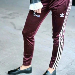 Adidas Track Pants i Burgundy-färg!! - Ännu ett par Adidas Track Pants-byxor i min samling som förtjänar att nyttjas vidare och oftare!  Dessa supercoola i burgundy-färg är sjukt snygga att matcha mellan olika stilar.  Färg: Burgundy/vinröd/lilaröda  Midja: 38 cm (medium) med stretch och 