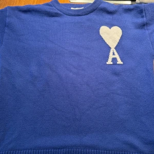 AMI Tröja Blå - Säljer en snygg blå stickad tröja med en vit hjärtdetalj(AMI) på bröstet. Tröjan har en klassisk rund hals och är perfekt för både höst och vinter. Den är väl använd! Inte säker på äkthet. Därav priset