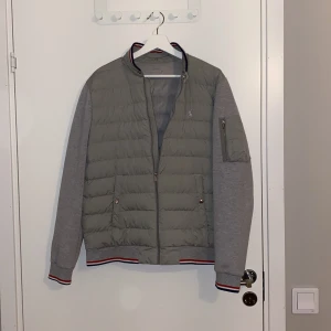 Grå jacka från Polo Ralph Lauren - Säljer en snygg grå jacka från Polo Ralph Lauren. Den har en quiltad design på framsidan och mjuka grå ärmar. Jackan har en dragkedja framtill och en praktisk ficka med dragkedja på ärmen. Den är i storlek M