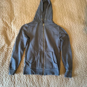 Mörkblå zipup från 157 - Säljer en grå hoodie från 157 i storlek XS. Den har en dragkedja framtill och en mysig huva. Perfekt för kyliga dagar eller som ett extra lager. Använd men i bra skick. Passar både till vardags och avslappnade tillfällen.
